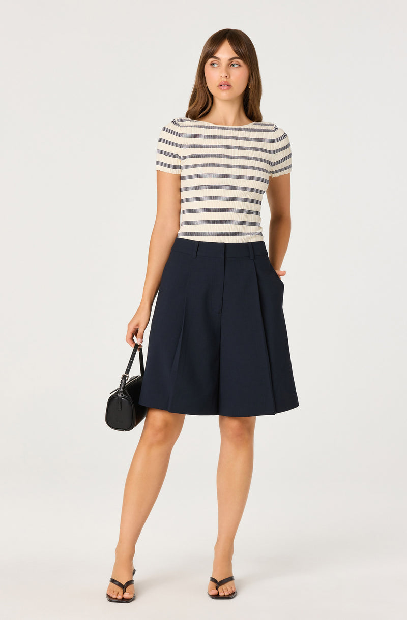 Woman wearing a striped short-sleeve top and navy pleated A-line skirt.