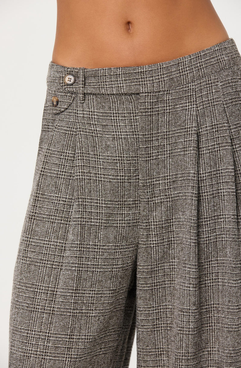 A person is wearing high-waisted, wide-leg pants with a brown and black plaid pattern. The pants have a front button closure with two visible buttons and a waistband that sits above the hips. The fabric features a classic checkered design with a textured appearance.
