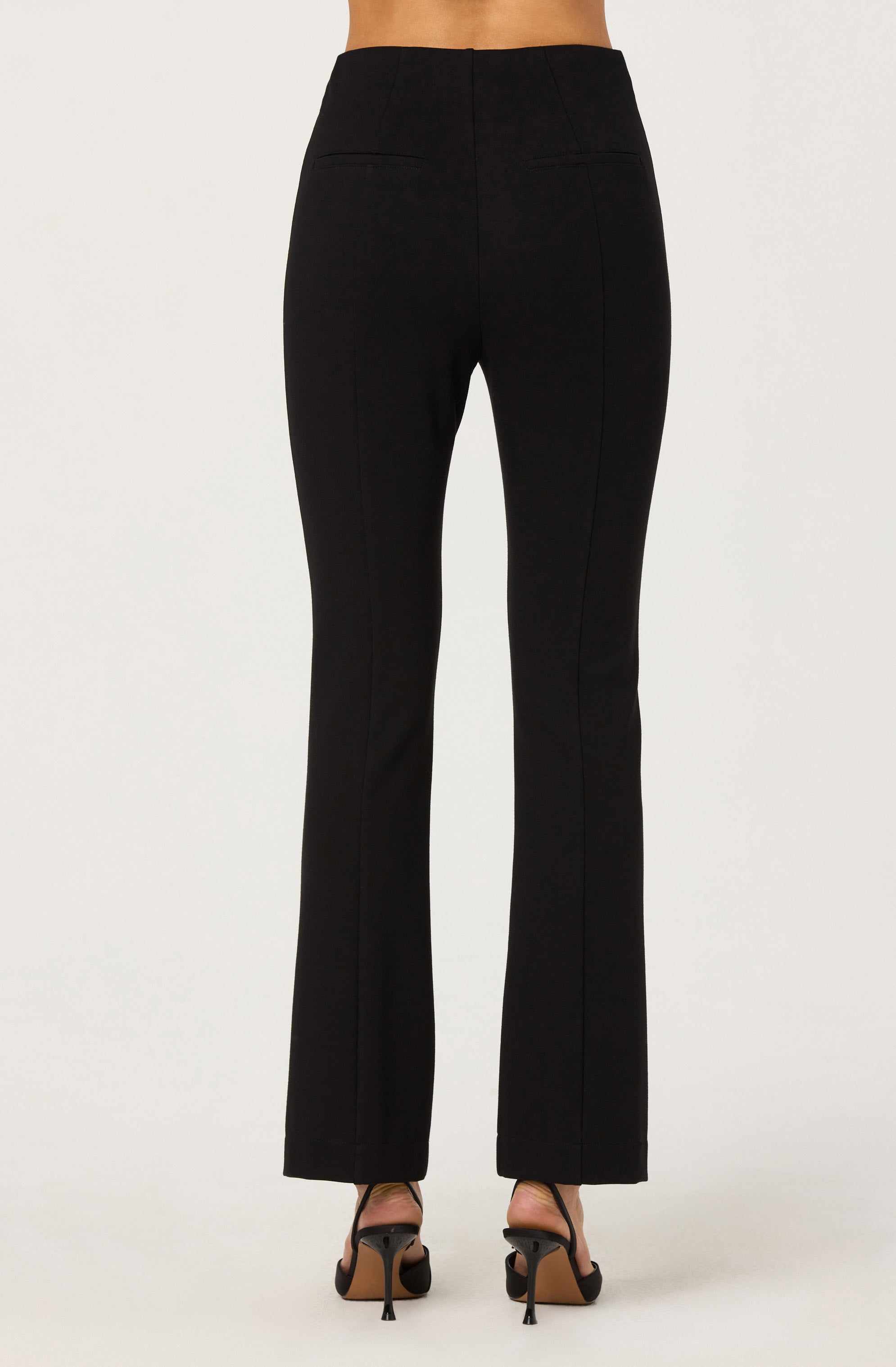 A person is wearing high-waisted black pants with a straight-leg fit that extend to the floor, paired with black high-heeled sandals. The pants have a smooth waistband without visible belt loops and appear to have a tailored fit.