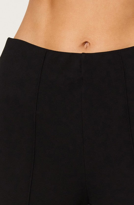 A person wearing a black high-waisted skirt with vertical seam lines. The skirt sits above the hips, exposing a small portion of the midriff and belly button. The fabric appears smooth and fitted.