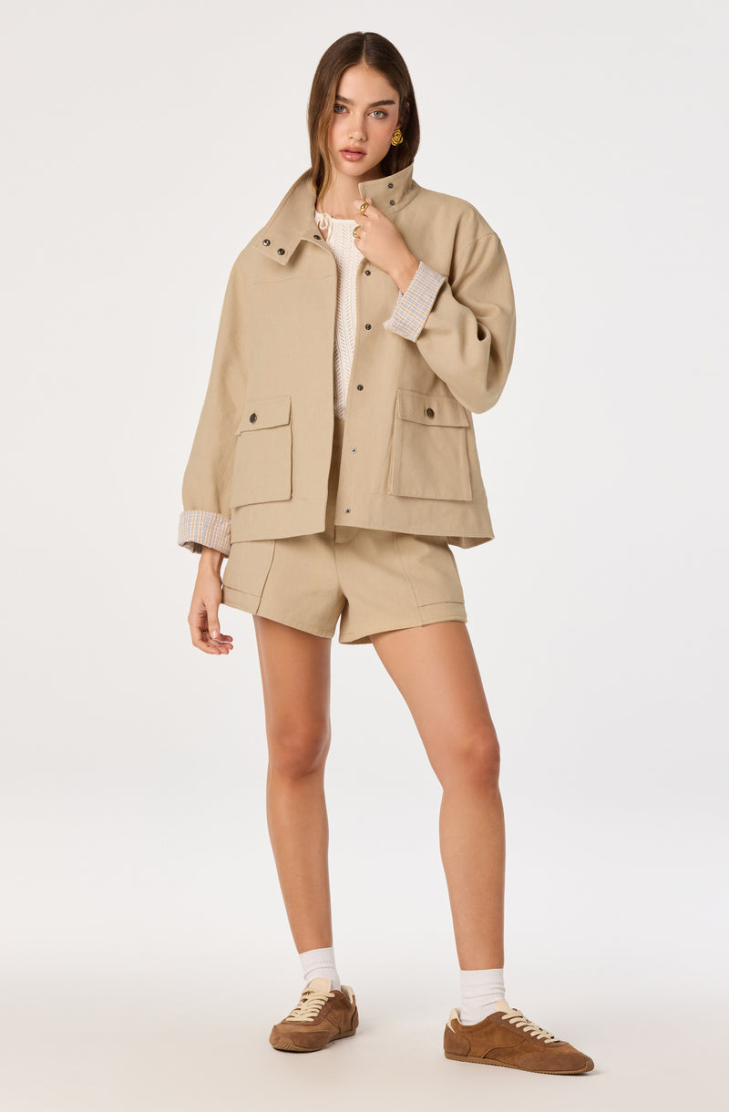 Beige oversized jacket with large front pockets, beige shorts, beige sneakers, and white socks.