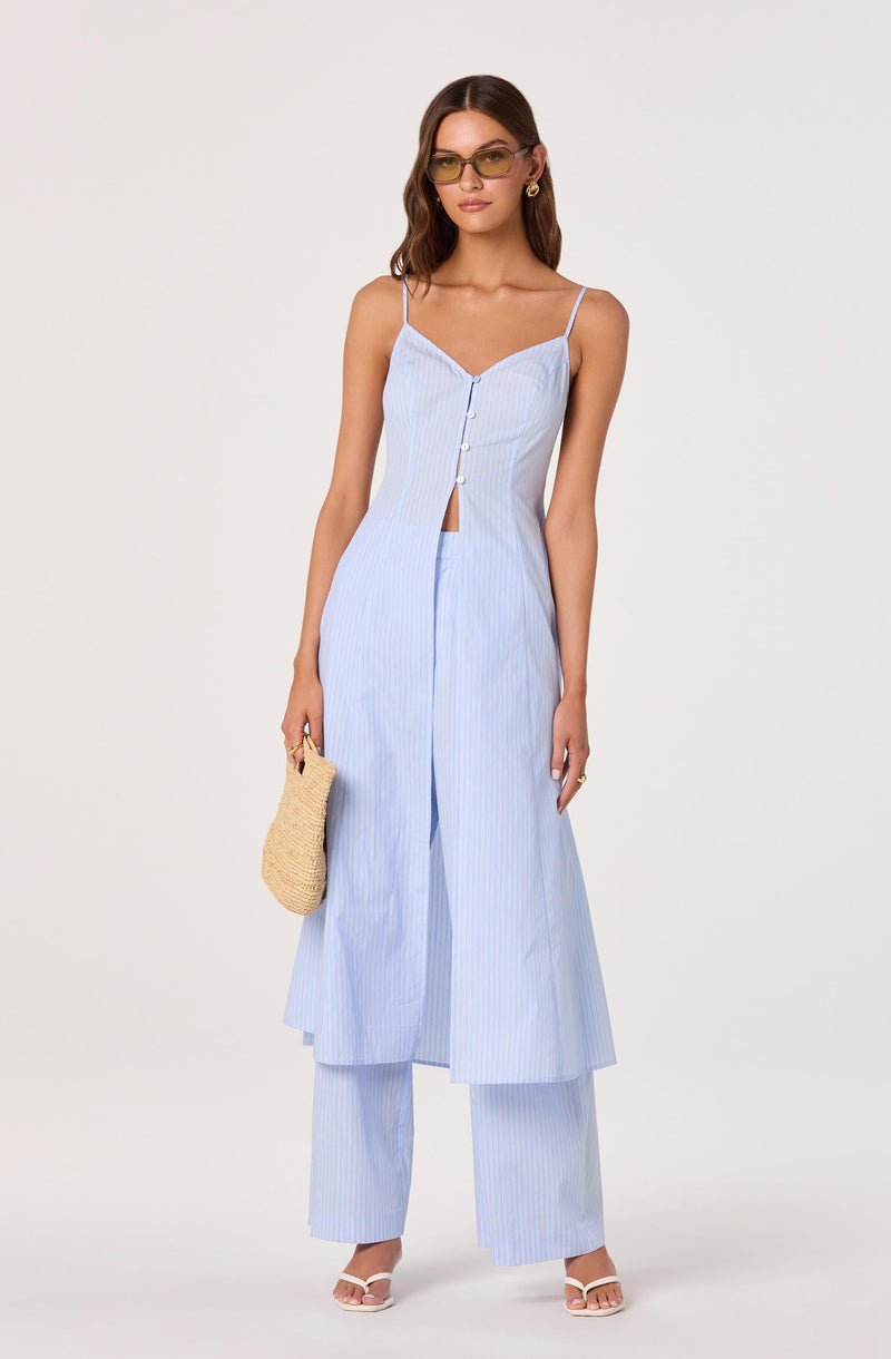Woman in light blue striped sleeveless top and matching wide-leg pants, holding a straw bag.