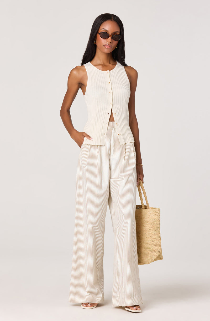 Woman wearing a sleeveless, cream-colored, vertically striped tank top and matching wide-leg pants.