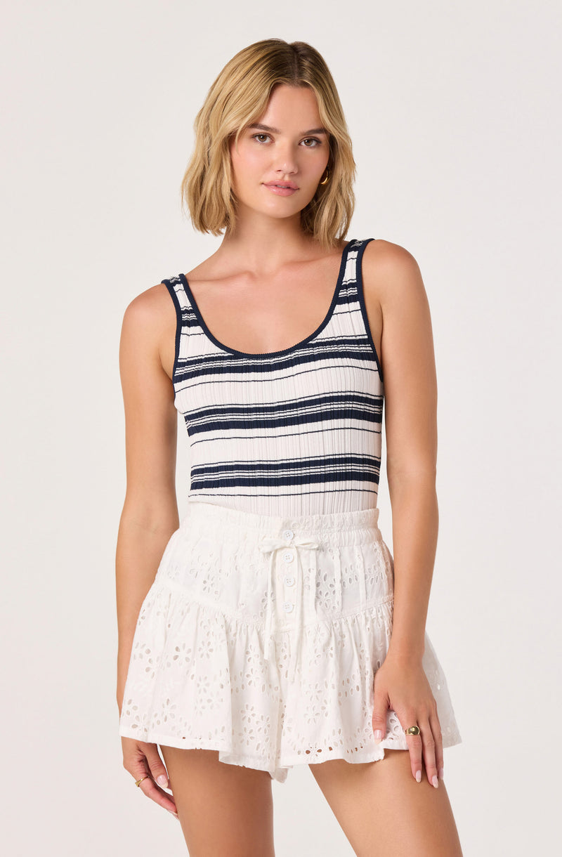 Woman wearing a sleeveless navy and white striped tank top and white eyelet skirt.