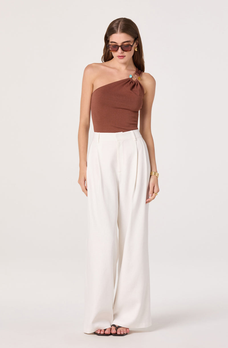 Woman wearing a one-shoulder brown top and high-waisted white wide-leg pants.