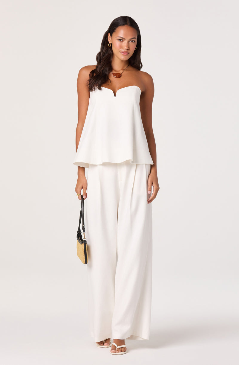 Woman in a white strapless top with a scalloped neckline and wide-leg white pants.
