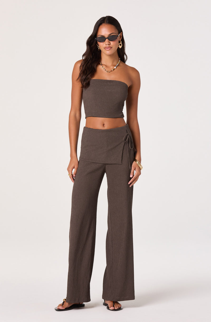 Woman wearing a strapless brown crop top and matching wide-leg pants with a tie detail.