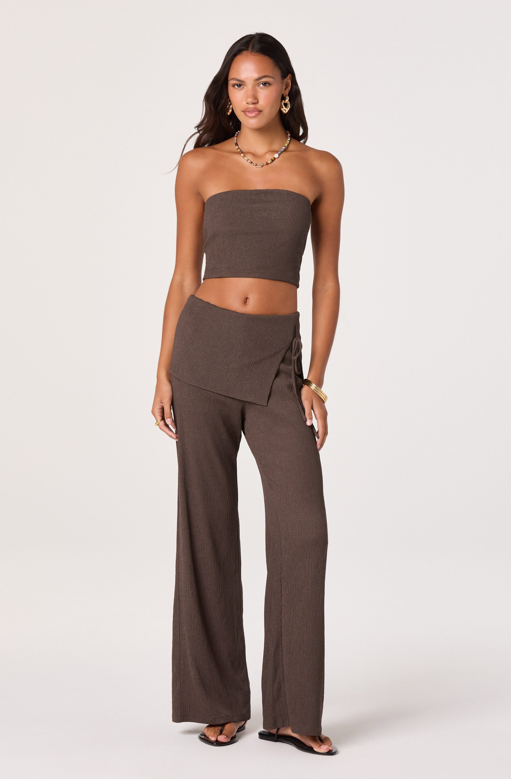 Woman in brown strapless top and matching wide-leg pants with a layered wrap detail.