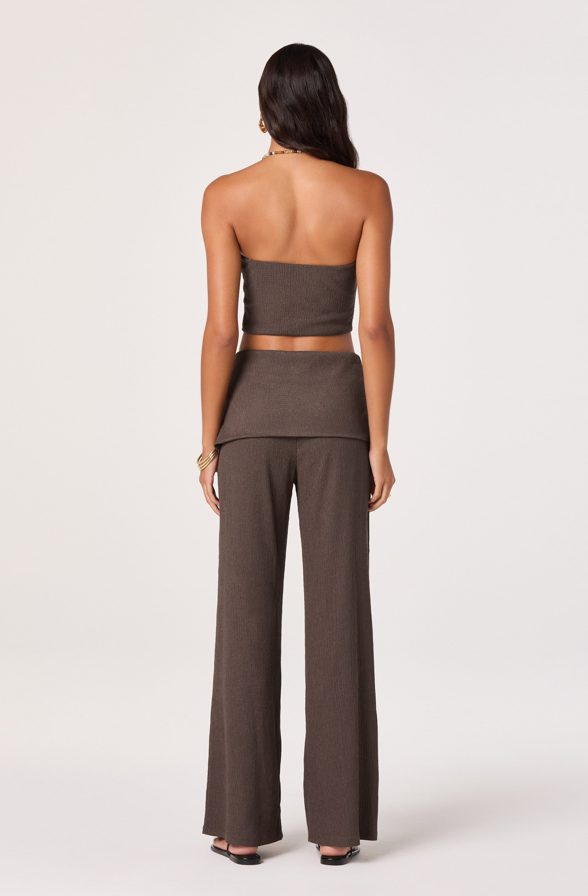 Woman wearing a strapless brown top and matching high-waist wide-leg pants.