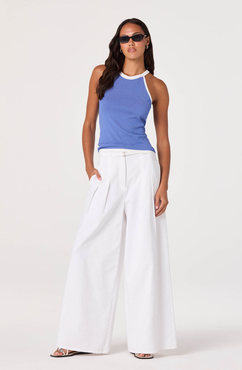 Woman wearing a sleeveless blue top with white trim and wide-leg white pants.