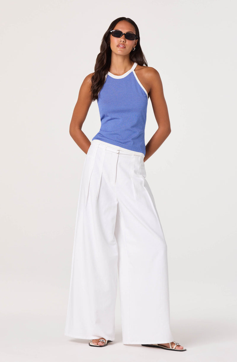 Woman in a blue sleeveless top and white wide-leg pants, wearing sunglasses.