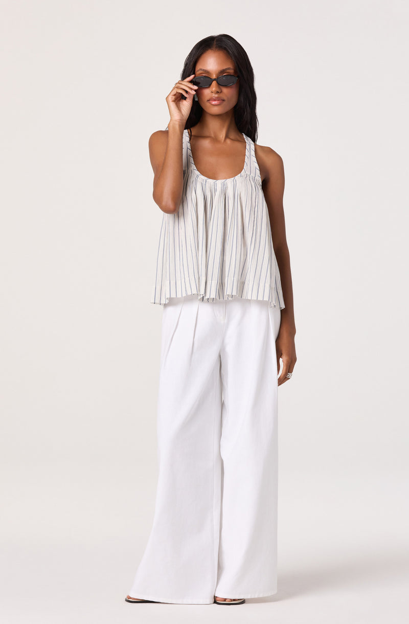 Woman in striped sleeveless top and wide-leg white pants, wearing sunglasses.