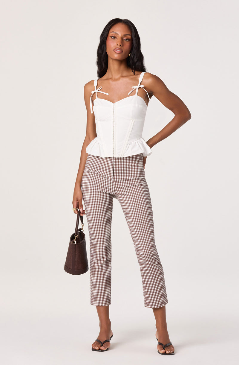 Woman wearing a white sleeveless top with tie straps and ruffled hem, checkered pants, and black open-toe heels.