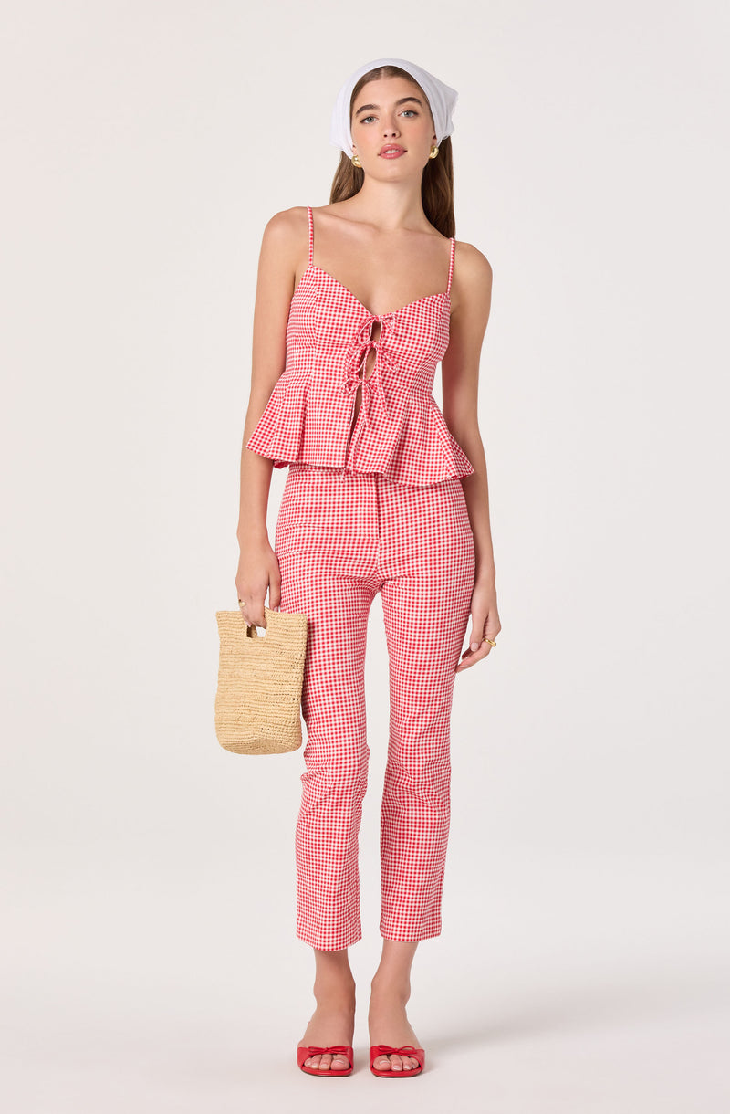 Girl in pink and white gingham top and pants, straw handbag, white headscarf, red sandals.