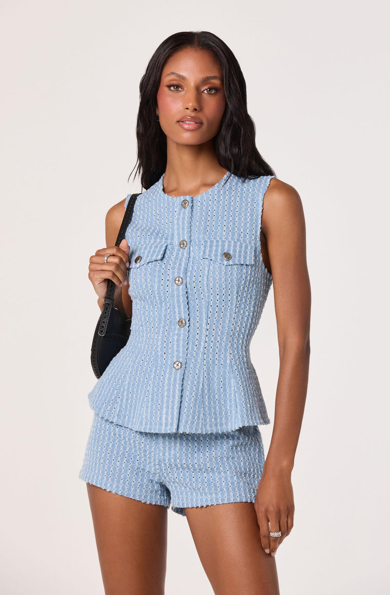 Woman wearing a sleeveless, light blue, textured matching top and shorts set with silver buttons