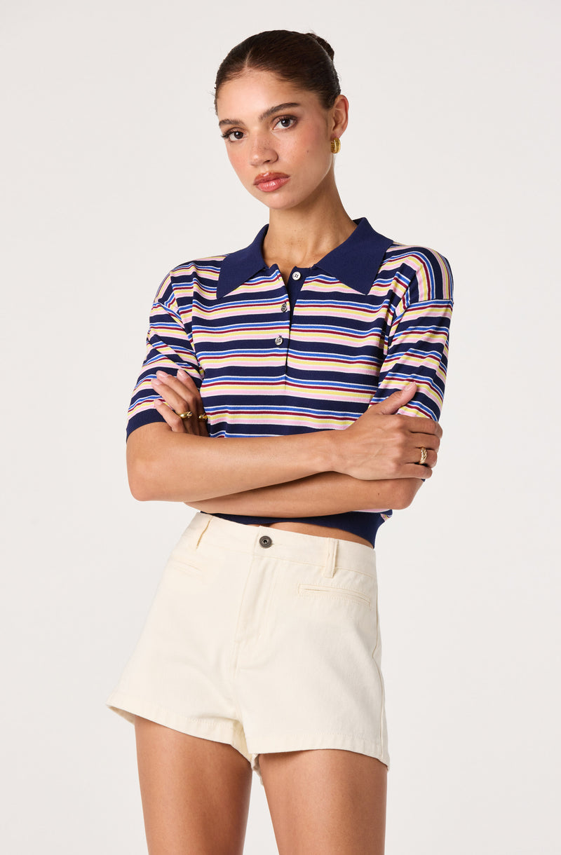 Woman wearing a multicolored striped polo shirt with a navy collar, paired with high-waisted off-white shorts.
