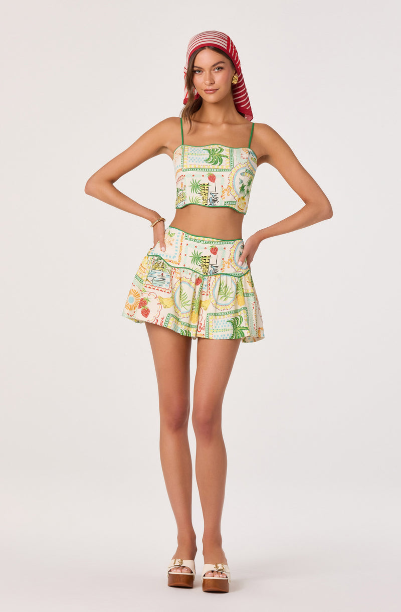 Girl wearing a colorful, patterned crop top and matching skirt with green straps, and a red and white striped headscarf.