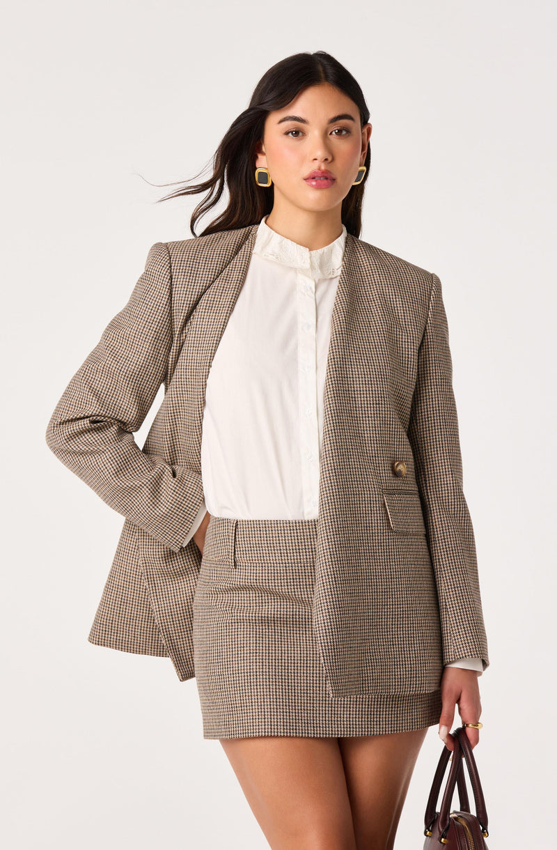 Woman in brown plaid blazer, matching plaid skirt, and white blouse against white background.