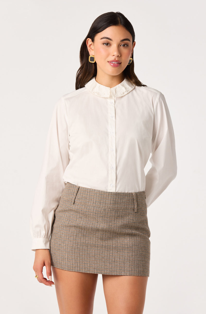 Woman wearing a white long-sleeve blouse with ruffled collar and a plaid mini skirt.