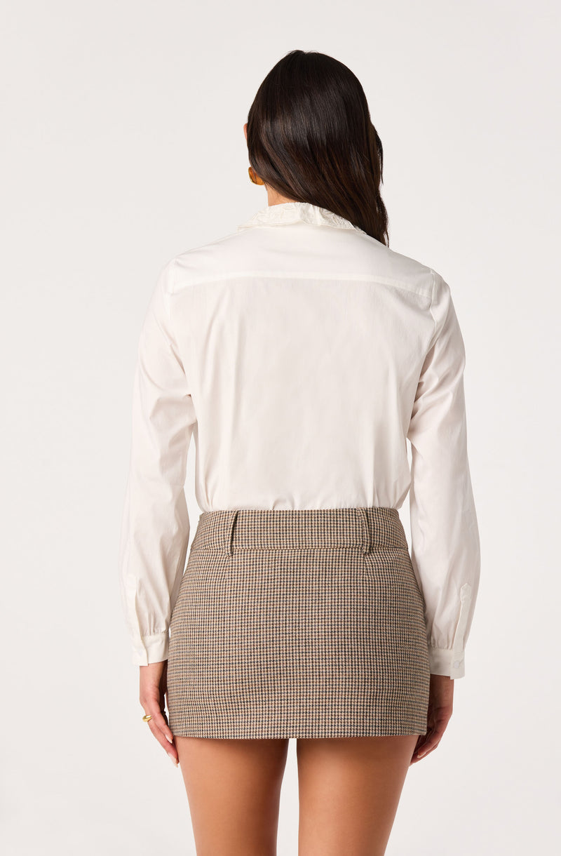 Woman in white blouse with ruffled collar and plaid mini skirt, facing away.