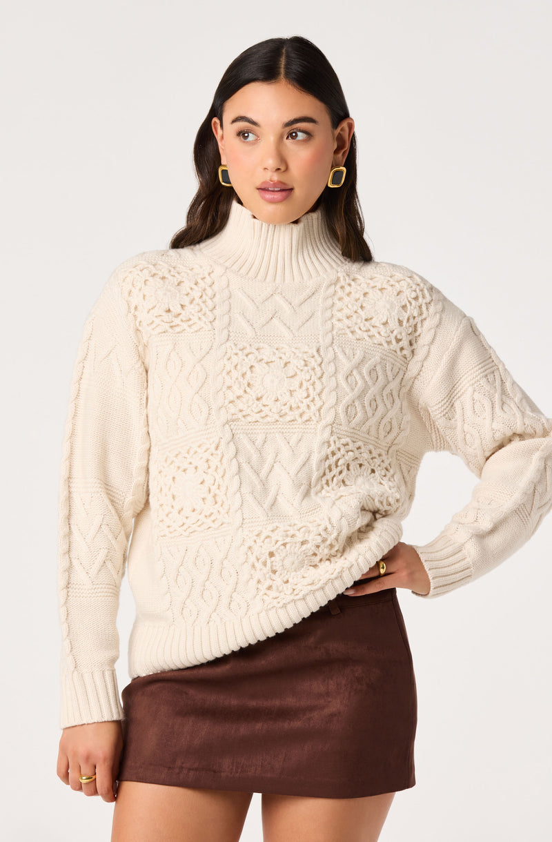 Woman wearing a cream chunky cable knit sweater with a high turtleneck and a brown leather mini skirt.