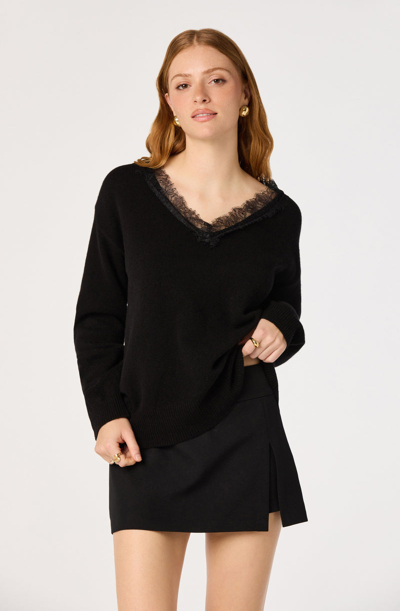 Black sweater with lace trim over the neckline, paired with a black skirt featuring a front slit.