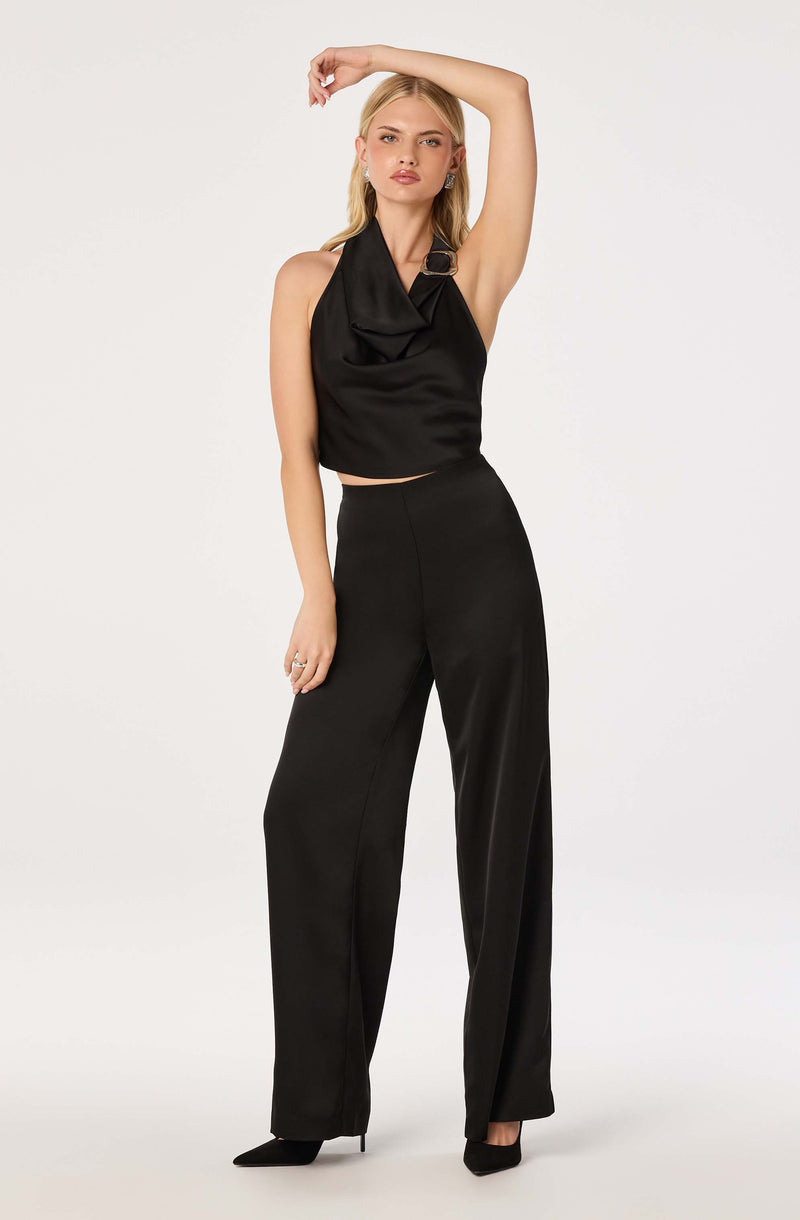 Woman wearing a sleeveless black satin top with a draped neckline and wide-leg black satin pants.