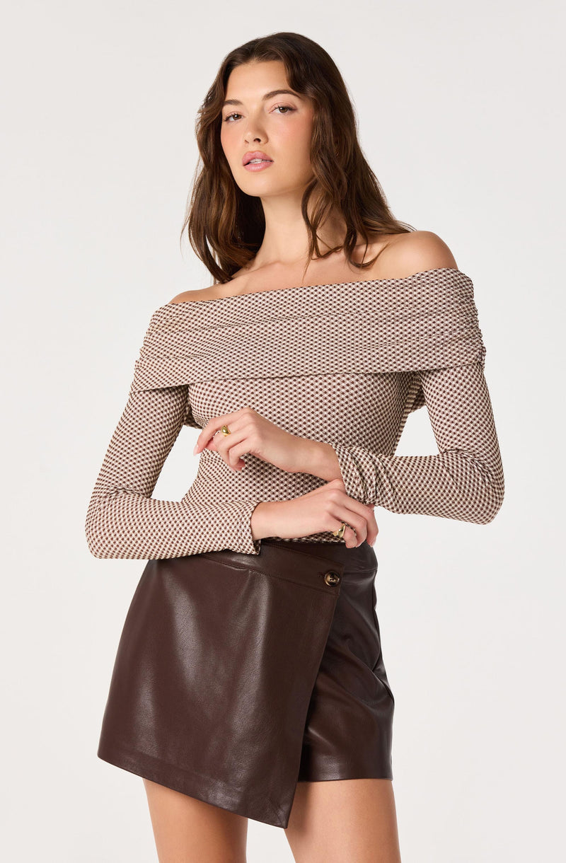 Woman wearing off-the-shoulder patterned top and a dark brown leather skirt.