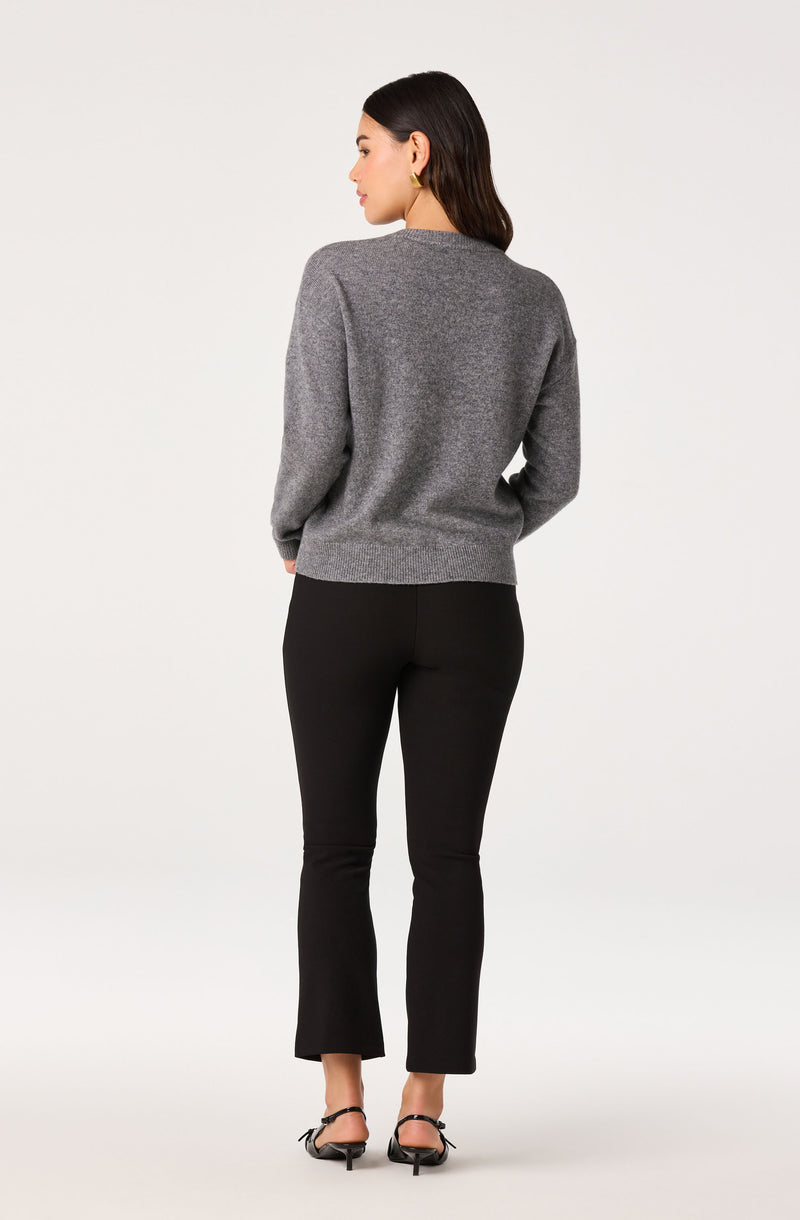 Woman in a gray sweater and black flared pants, black heels, facing away.