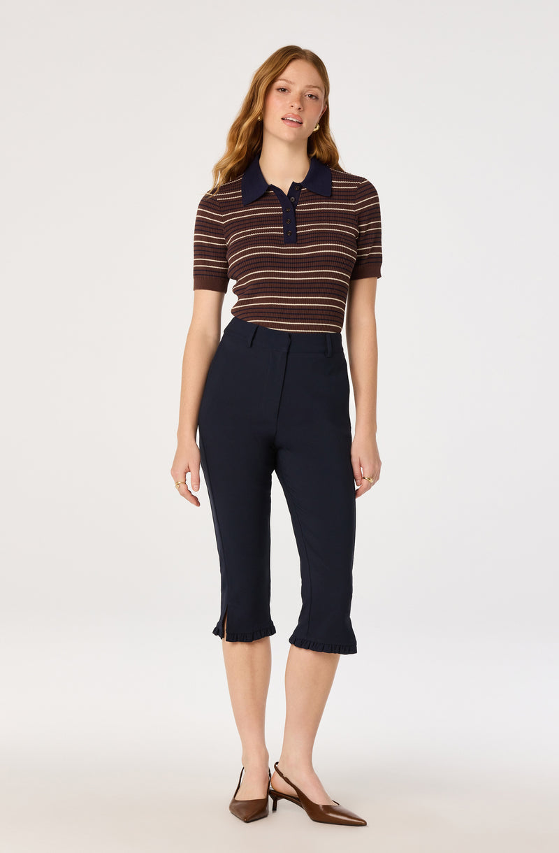 Woman wearing a short-sleeve, multicolored striped polo shirt with a navy collar and buttons, paired with dark cropped pants with ruffled hems.