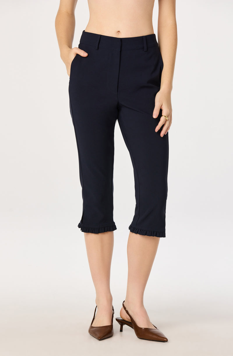 Woman wearing navy cropped pants with ruffled hems and brown heels.