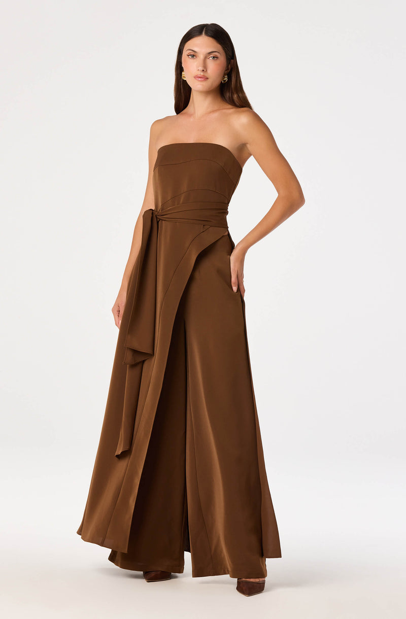 Brown strapless jumpsuit with wide-leg pants and a matching fabric belt tied at the waist.