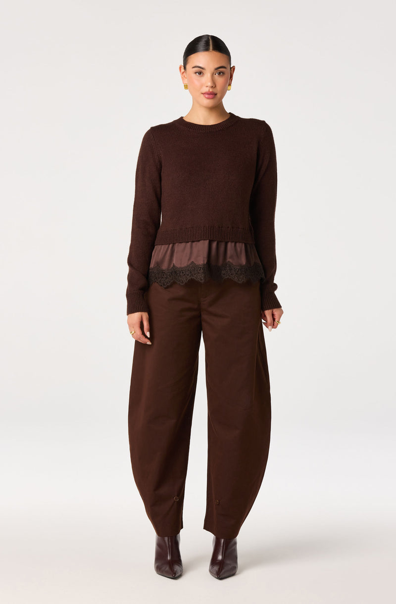 Woman wearing a dark brown sweater with a ruffled, transparent, brown fabric and lace hem, paired with matching wide-legged pants and brown ankle boots.