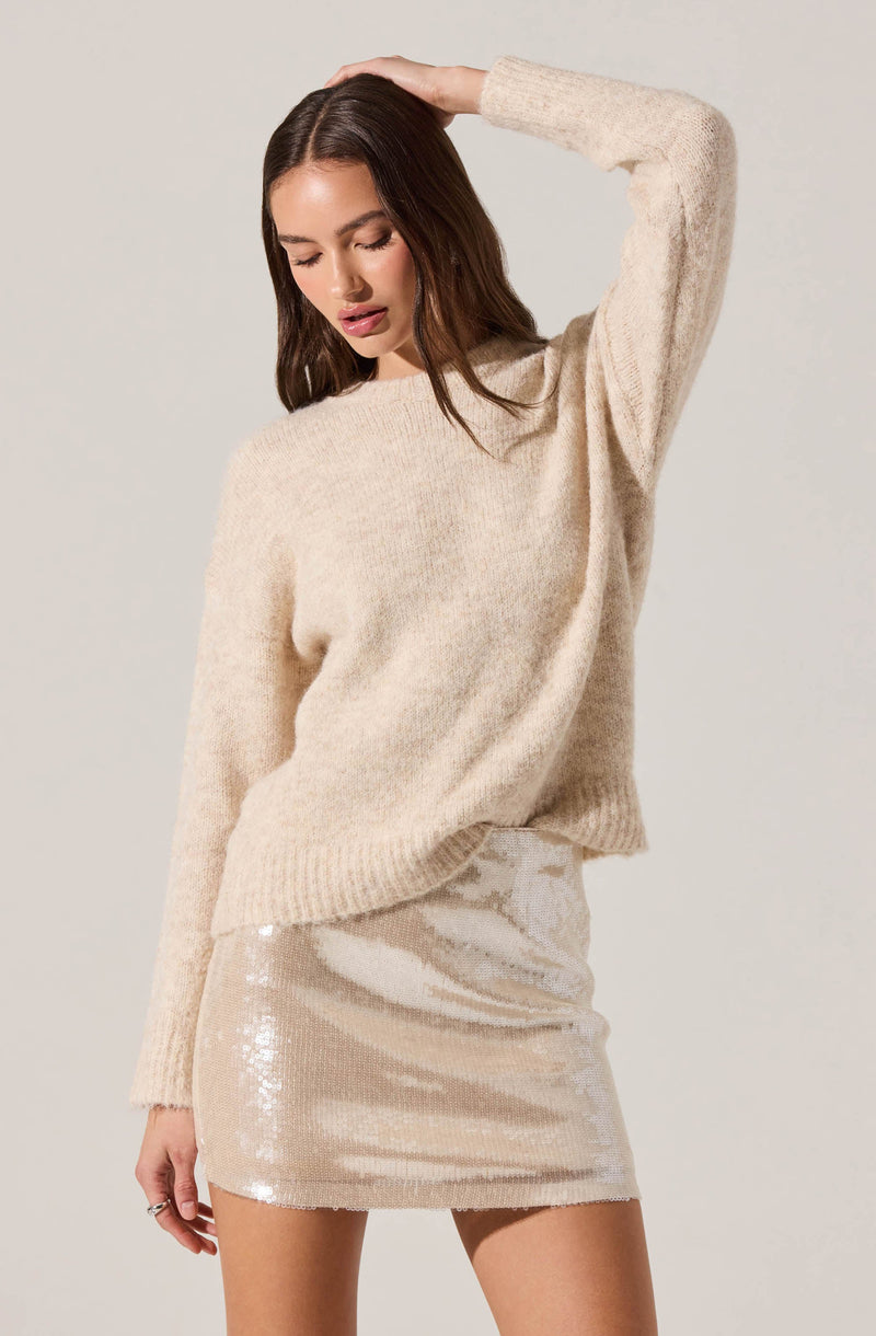 A woman is wearing a loose-fitting, long-sleeved, beige knit sweater with a round neckline. She pairs it with a shiny, sequined beige mini skirt.