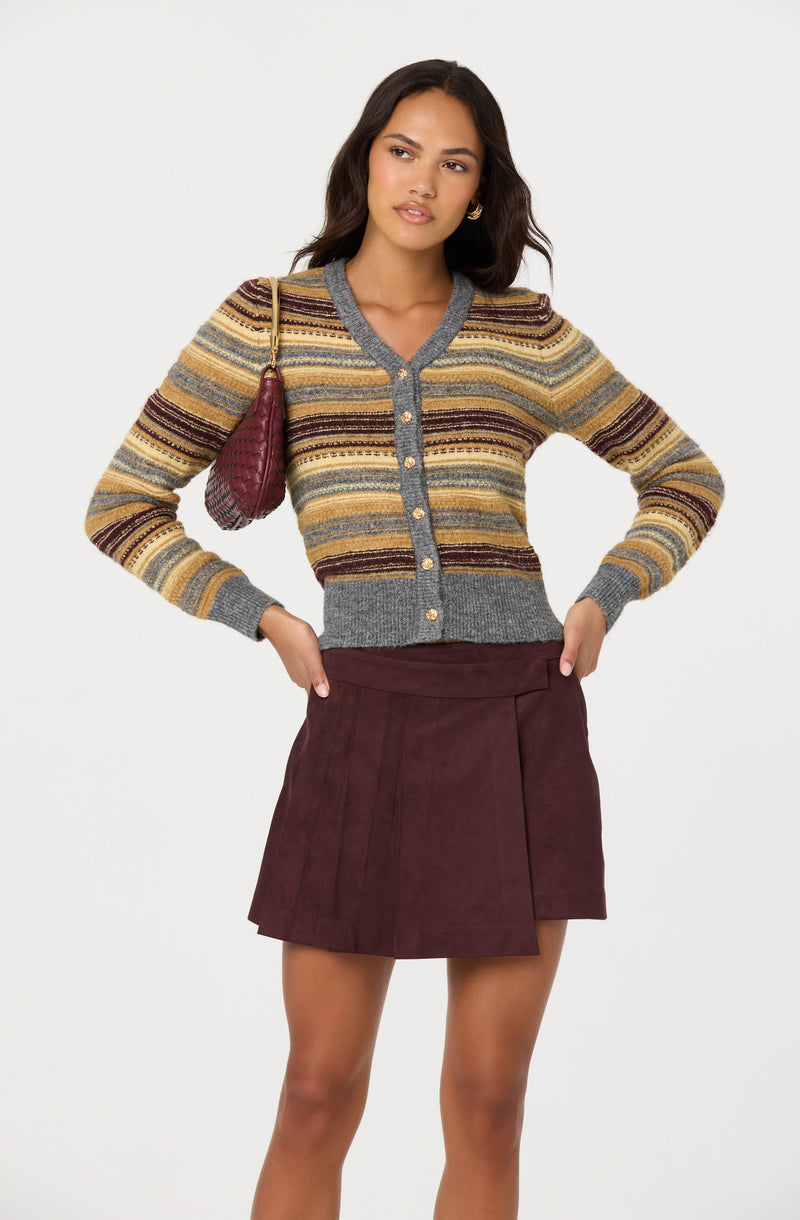 Woman wearing a multicolored striped cardigan and a burgundy skirt, carrying a matching burgundy bag.