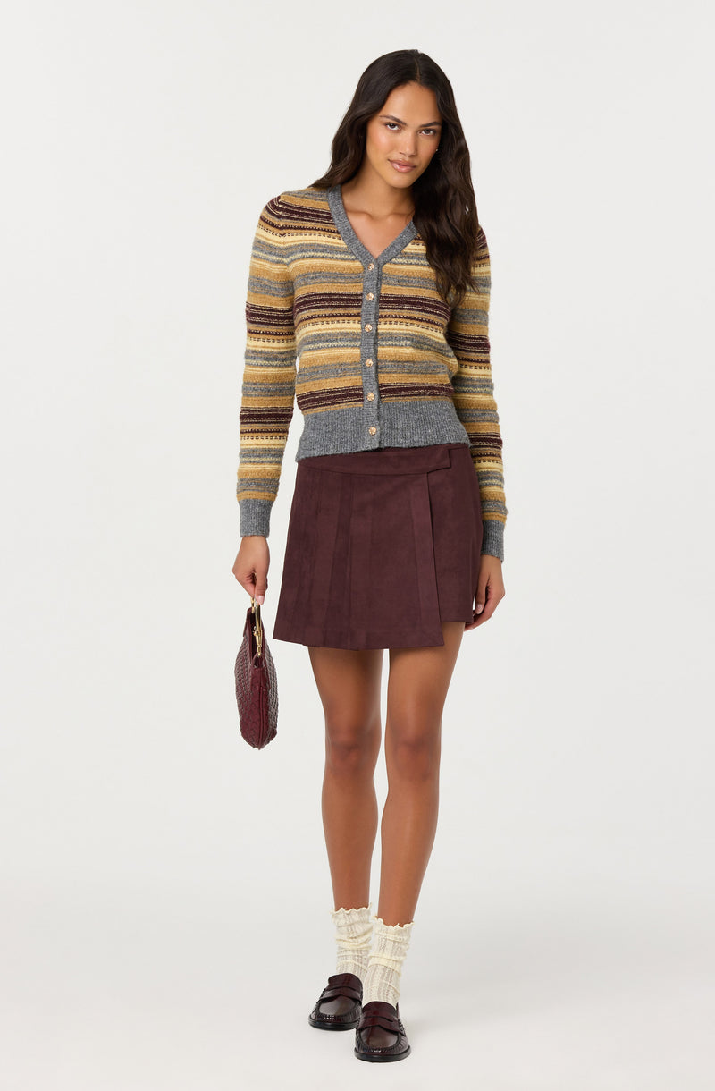 Model wearing a multicolored striped cardigan, maroon skirt, cream socks, and maroon shoes, holding a burgundy purse.