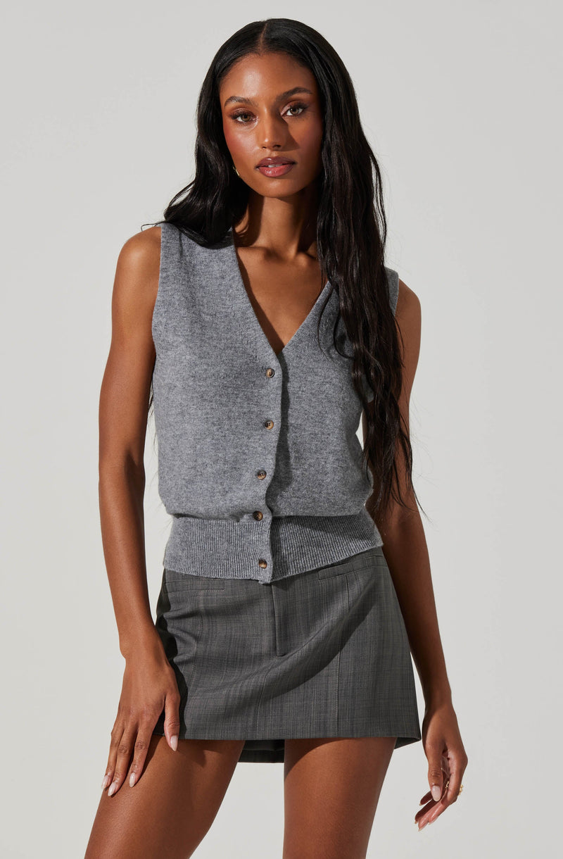 A woman is wearing a sleeveless, gray knit vest with a V-neckline and button-up front, paired with a gray plaid mini skirt.
