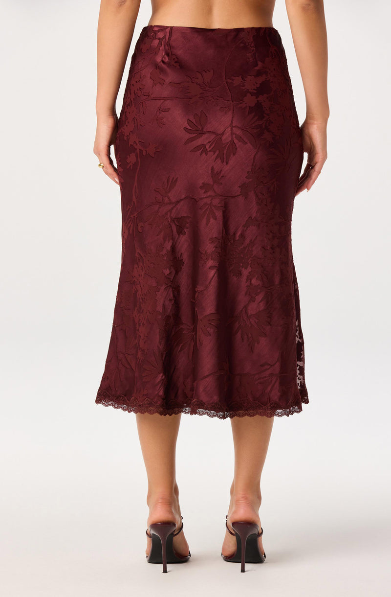 Burgundy satin midi skirt with a floral jacquard pattern and lace hem, worn with high heels.