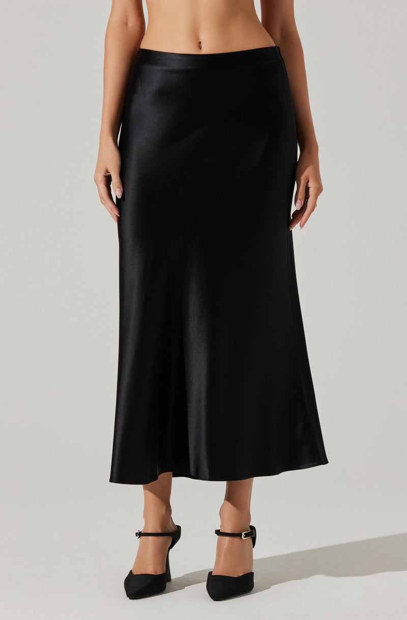 A woman is wearing a long, black satin skirt that reaches her ankles. She is also wearing black high-heeled shoes with ankle straps. The skirt has a smooth, shiny texture and a simple, elegant design.