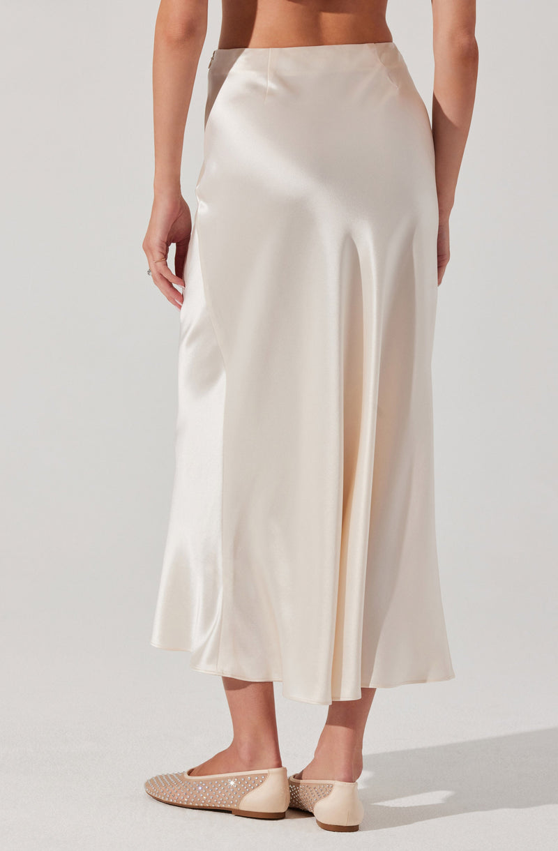 A person is wearing a high-waisted, full-length cream satin skirt with a smooth, shiny finish. They are also wearing beige flats with a decorative pattern of small, shiny embellishments.