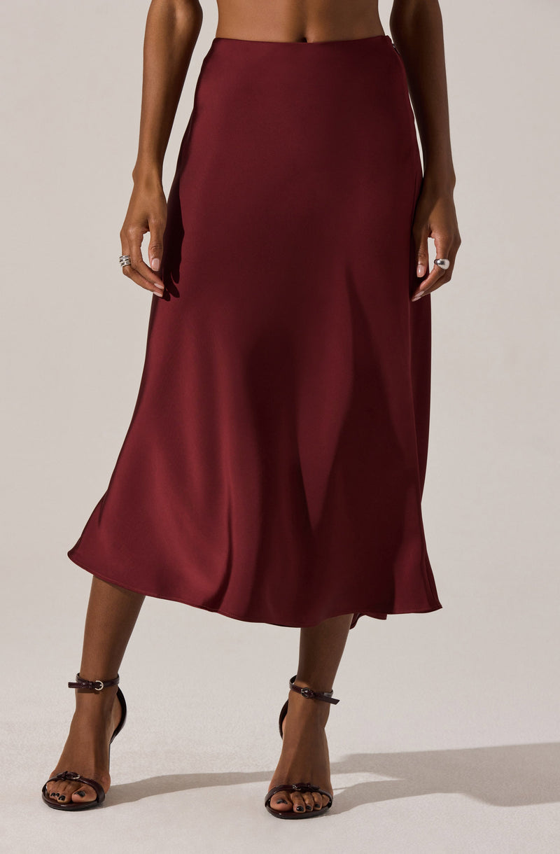A woman is wearing a high-waisted, ankle-length satin skirt in a deep burgundy color. She is also wearing black strappy high-heeled sandals.
