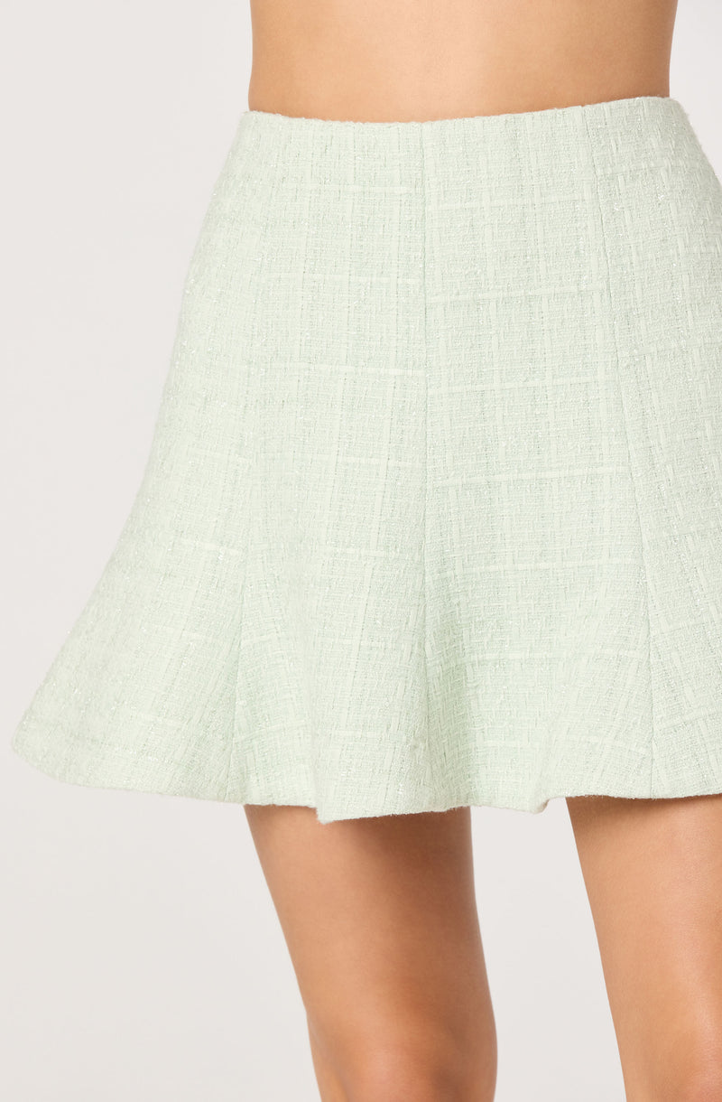 A model wearing a light-colored, textured, high-waisted, A-line skirt that falls above the knees. The fabric has a woven, slightly rough appearance with subtle vertical and horizontal lines, giving it a classic and elegant look.