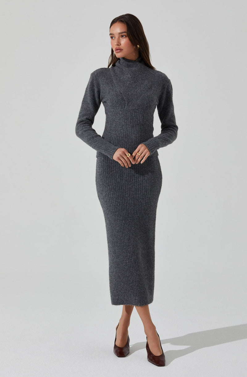 A woman wearing a fitted, long-sleeved, dark gray knit dress with a high neckline. The dress is ribbed and extends down to her ankles. She is also wearing dark brown high heels.