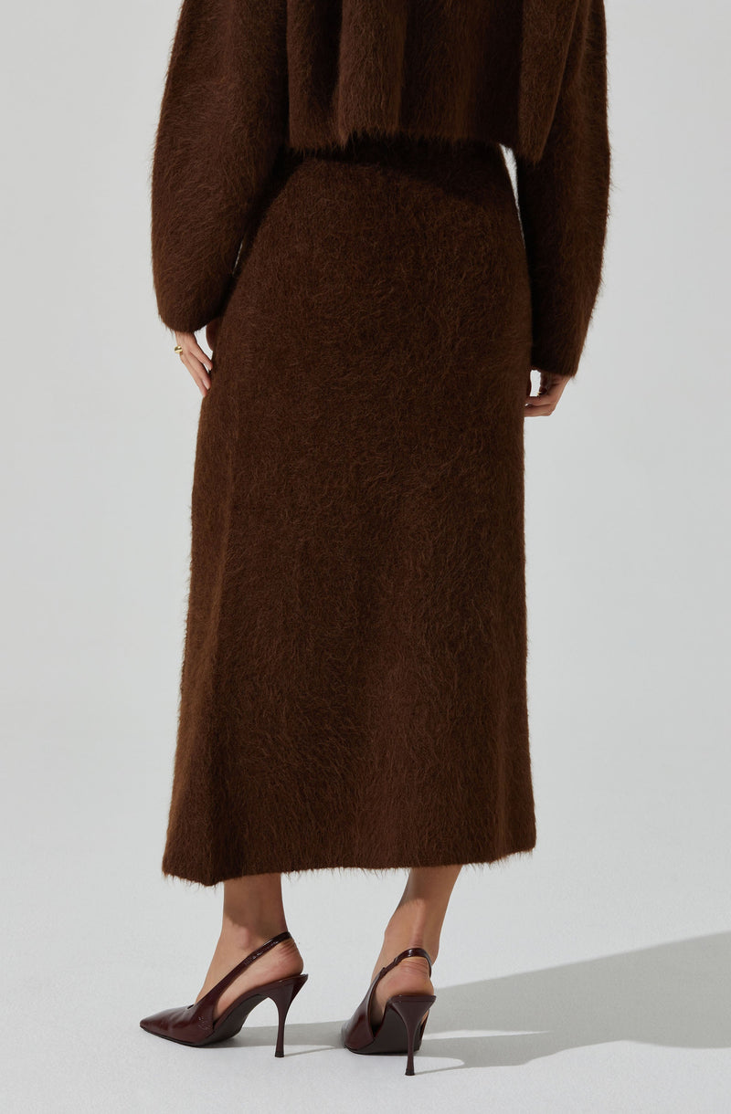 A person is wearing a long, brown, fuzzy skirt that reaches the ankles. They are also dressed in a matching brown, fuzzy top with long sleeves. The outfit appears cozy and warm, with the top slightly loose-fitting. The person is wearing brown high-heeled shoes with pointed toes and ankle straps.