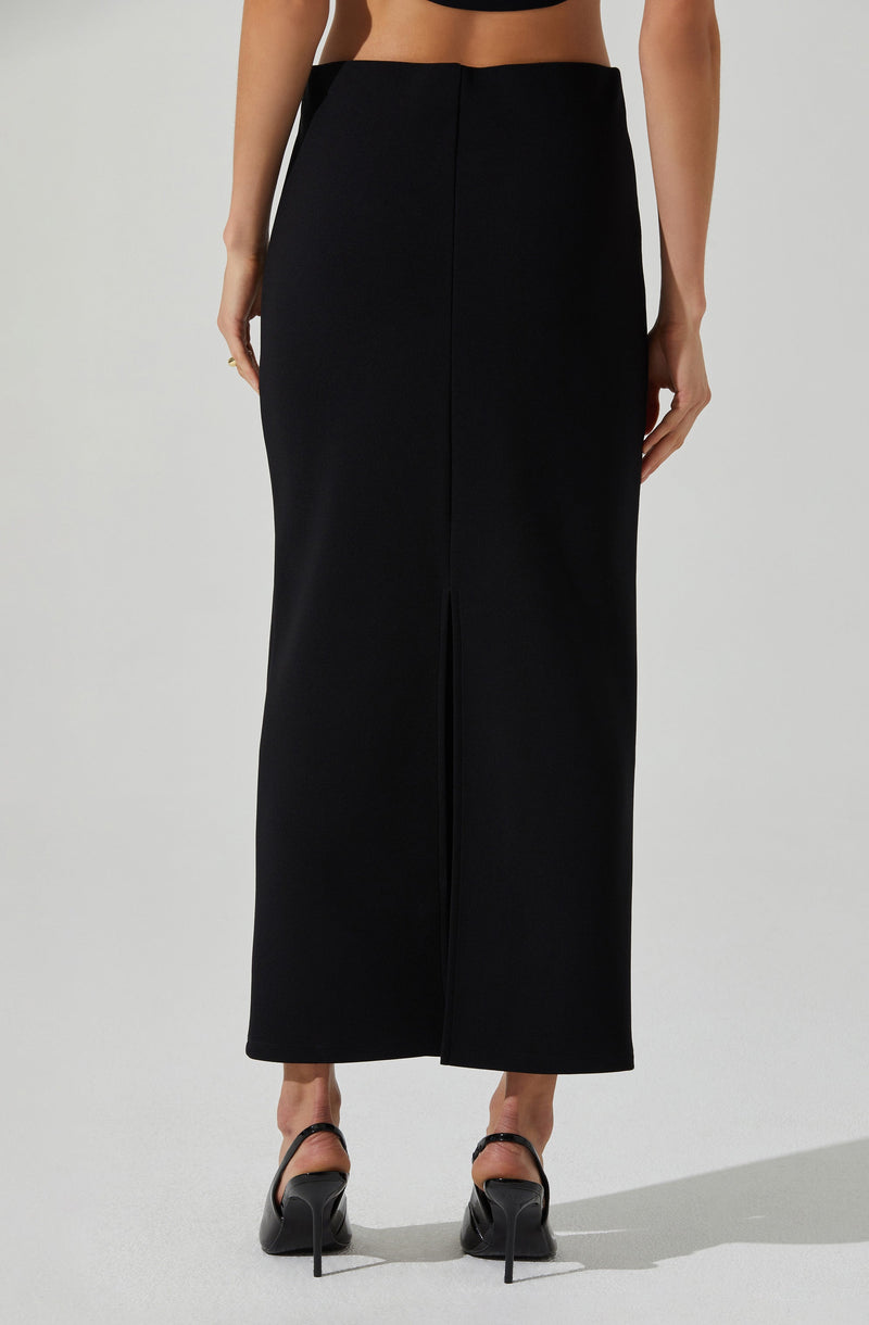 A woman is wearing a high-waisted, wide-leg black skirt that extends to her ankles. She has paired it with black high-heeled shoes with ankle straps. The skirt has a central front slit and is made of a smooth, slightly shiny fabric.