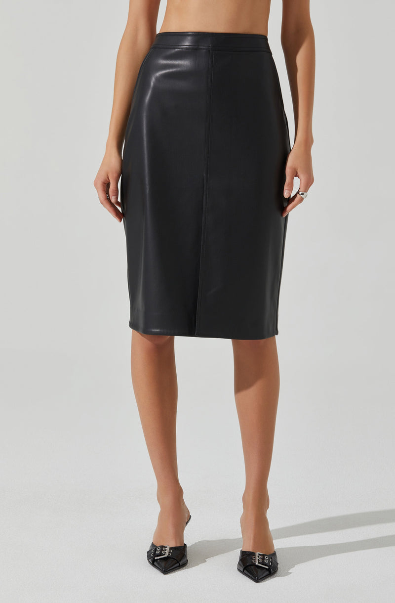 A woman is wearing a black leather midi skirt with a high waist and a straight, slim fit. She is also wearing black pointed-toe heels with decorative silver buckle details.