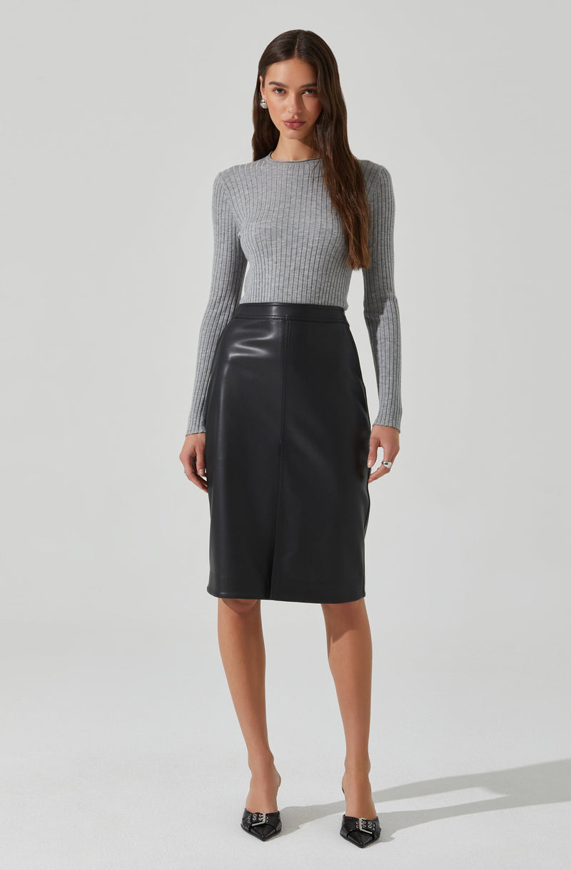 A woman is wearing a fitted, long-sleeved, ribbed knit sweater in light gray. She pairs it with a high-waisted, knee-length black leather skirt that has a sleek, slightly A-line silhouette. She completes the outfit with pointed black heels and pearl earrings.