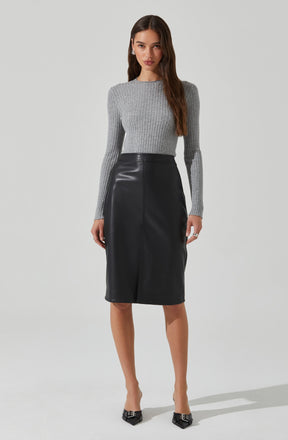 A woman is wearing a fitted, long-sleeved, ribbed knit sweater in light gray. She pairs it with a high-waisted, knee-length black leather skirt that has a sleek, slightly A-line silhouette. She completes the outfit with pointed black heels and pearl earrings.