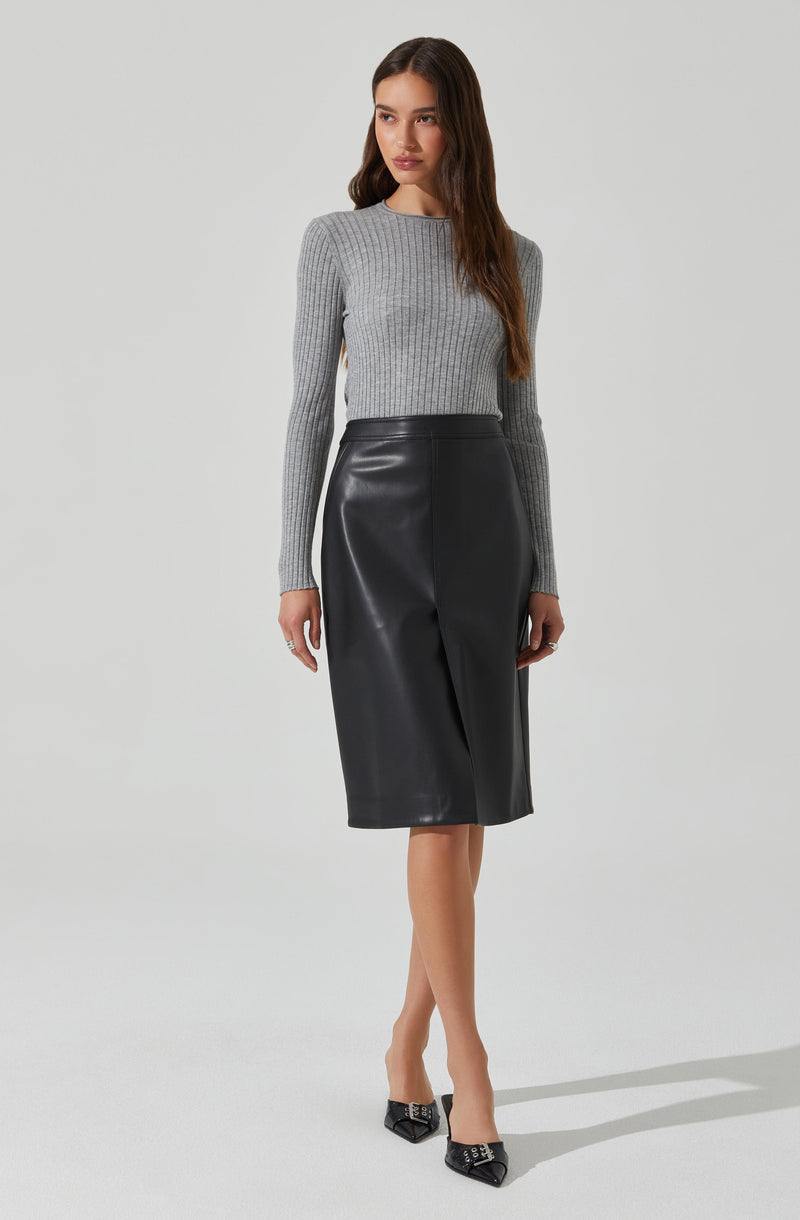 A woman is wearing a fitted, long-sleeved, ribbed gray sweater with a round neckline. She pairs it with a high-waisted, black leather midi skirt that falls below her knees. She completes the outfit with pointed black high heels featuring a decorative embellishment on the toe.