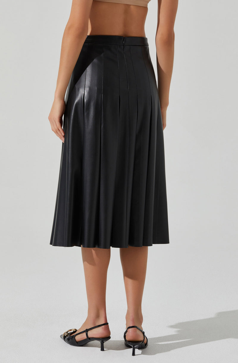 A woman is wearing a high-waisted, black, midi-length skirt made of shiny leather material. The skirt features pleats that add volume and texture to the design. She is also wearing a beige crop top and black strappy heels with a small heel and gold embellishments.